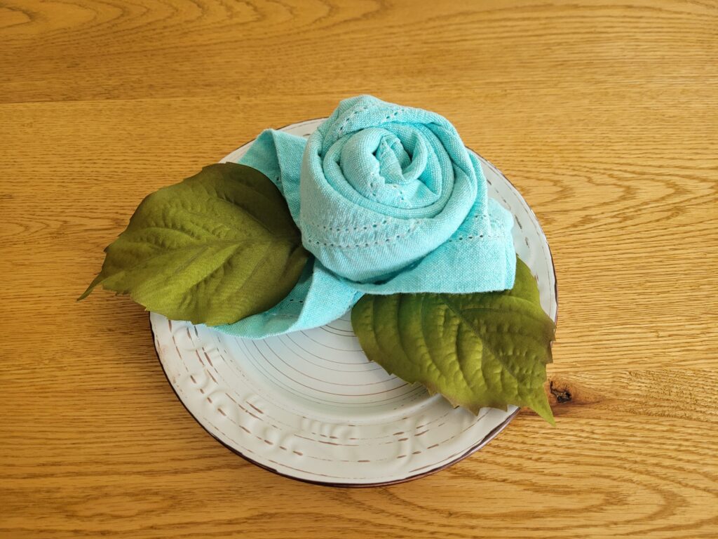 Napkin rose on a plate with green silk leaves