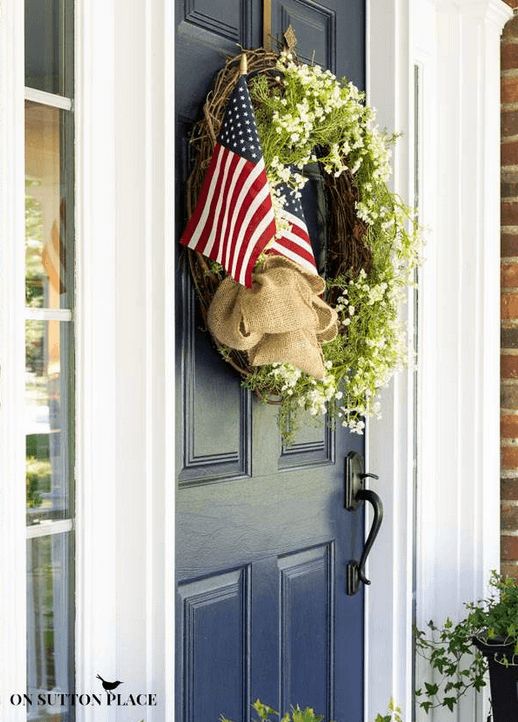 Grapevine wreath with tiny white flowers and two American flags on a dark blue front door