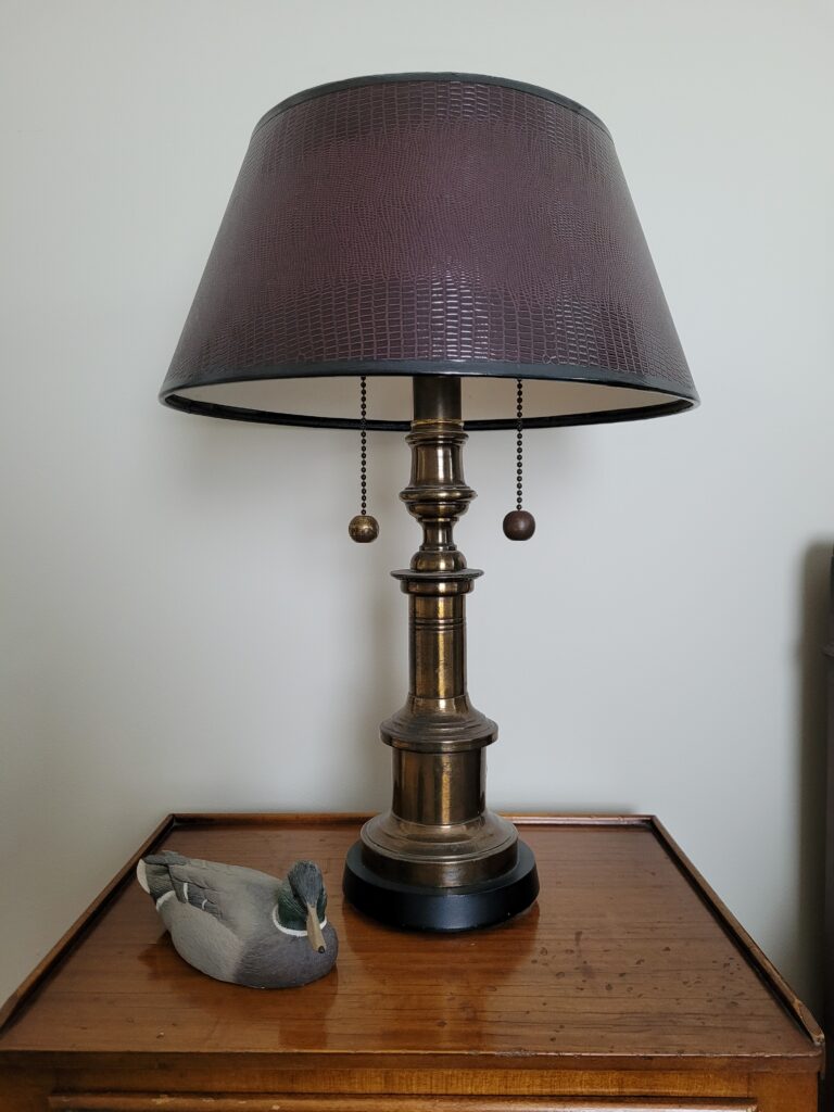 Image of nightstand with a brass lamp and small duck decoy sitting on it.