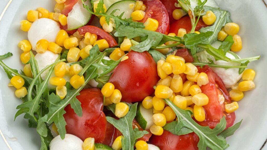 Caprese corn salad with arugula in a white bowl