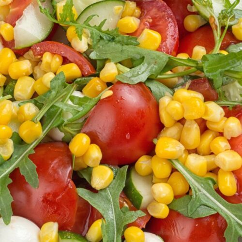 Caprese corn salad with arugula in a white bowl