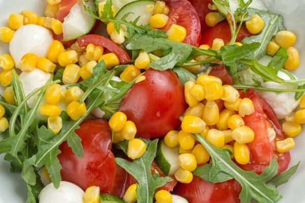 Caprese corn salad with arugula in a white bowl