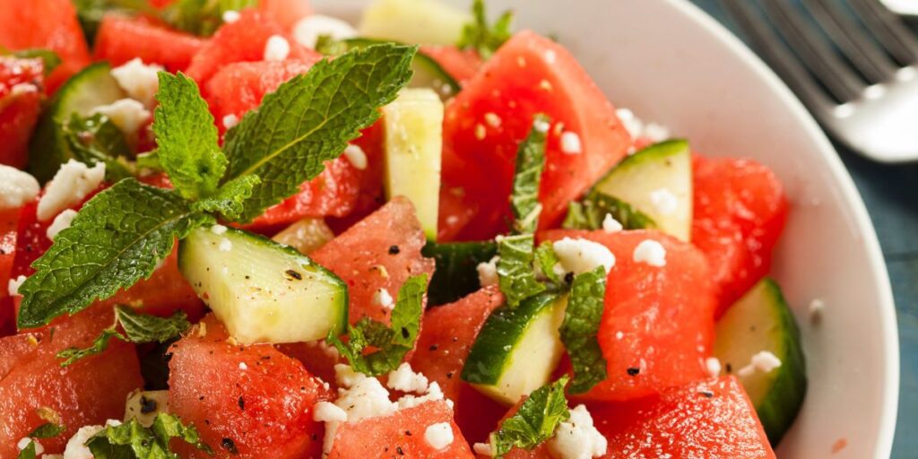 Cucumber watermelon salad garnished with mint leaves and topped with feta cheese crumbles in a white bowl.