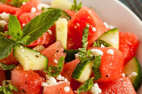 Cucumber watermelon salad garnished with mint leaves and topped with feta cheese crumbles in a white bowl.