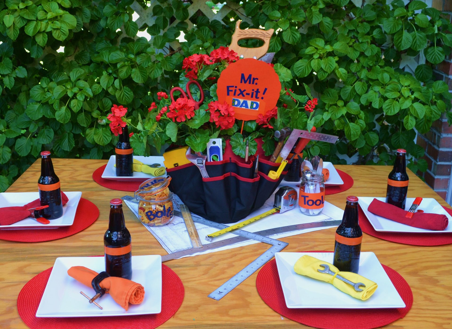 A tablescape featuring a toolbelt centerpiece filled with hand tools and red geraniums.