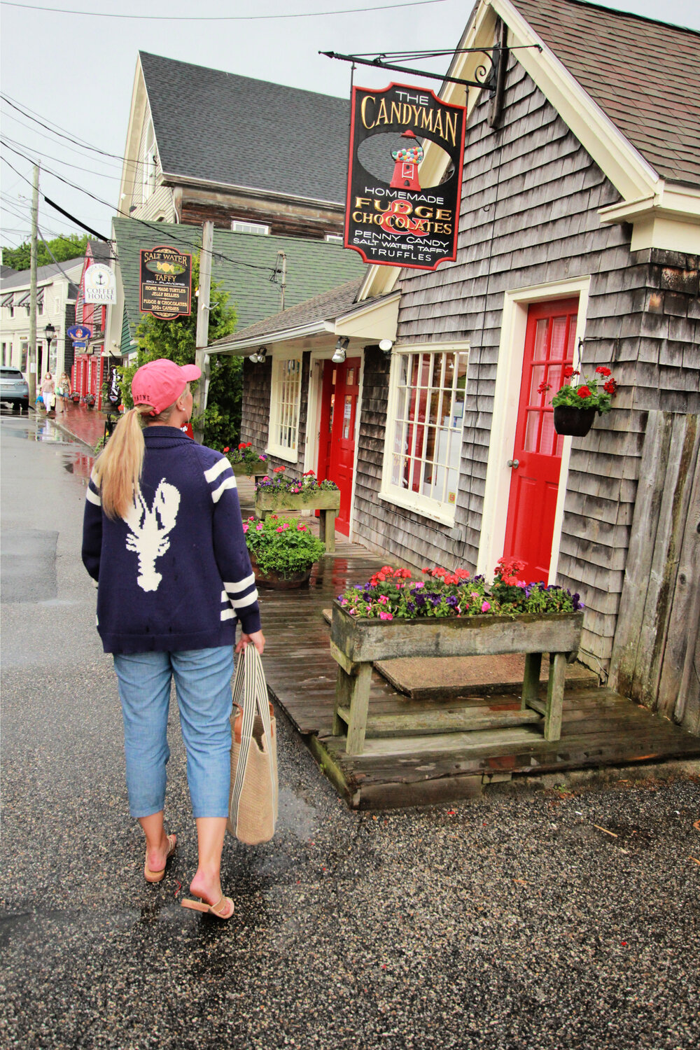 Photo of woman in denim Capri pants, Jack Rogers sandals, and a dark blue sweater with a white lobster carrying a tote bag in town in Kennebunkport.