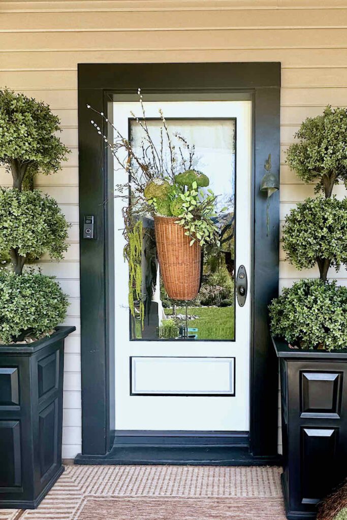 Large vintage basket filled with moss mushrooms and balls, greenery, and pussy willow stems hanging on a glass door window.