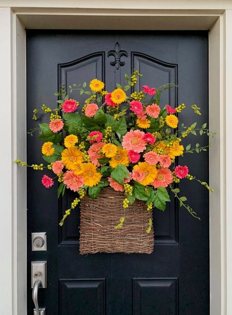 Large basket of gerbera daisies in yellow, coral, and pink hanging on a black door.