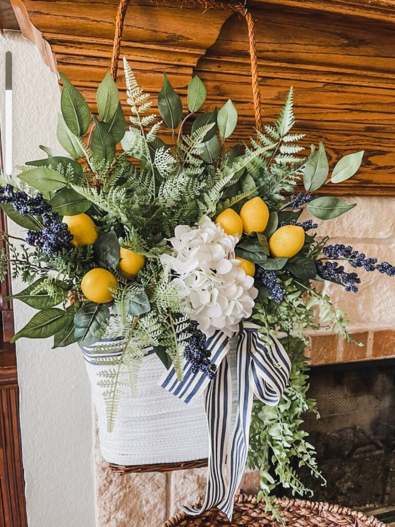 Basket covered in white jute rope filled with white hydrangea, lemons, blackberries, and greenery hanging on a wood fireplace mantle.