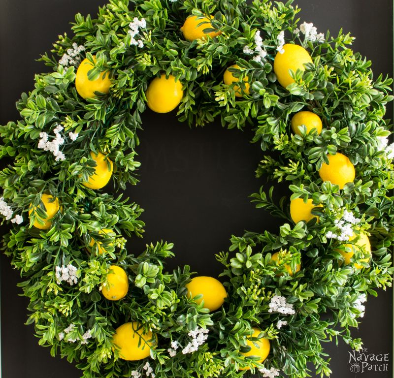 Boxwood wreath with lemons hanging on a black door.