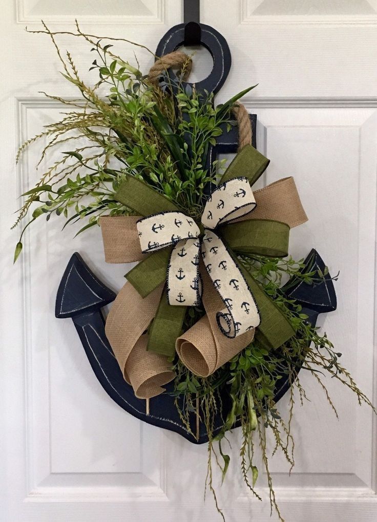 Dark blue wood anchor decorated with faux grasses and a big bow hanging on a white door.