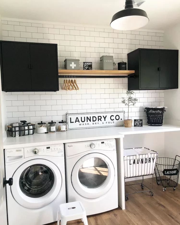 Farmhouse-style laundry room in black and white with a wood floor. A black tension rod was installed under a wood shelf separating two black upper cabinets over the washer and dryer.