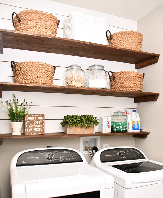 Shiplap wall above a white washer and dryer with three wood shelves.