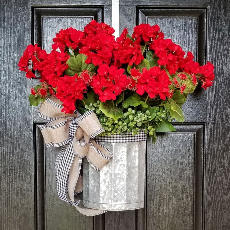 Bucket with red geraniums and a bow hanging on a black door.