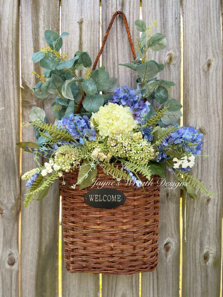 Basket of blue and cream hydrangeas with eucalyptus hanging on a wood fence.