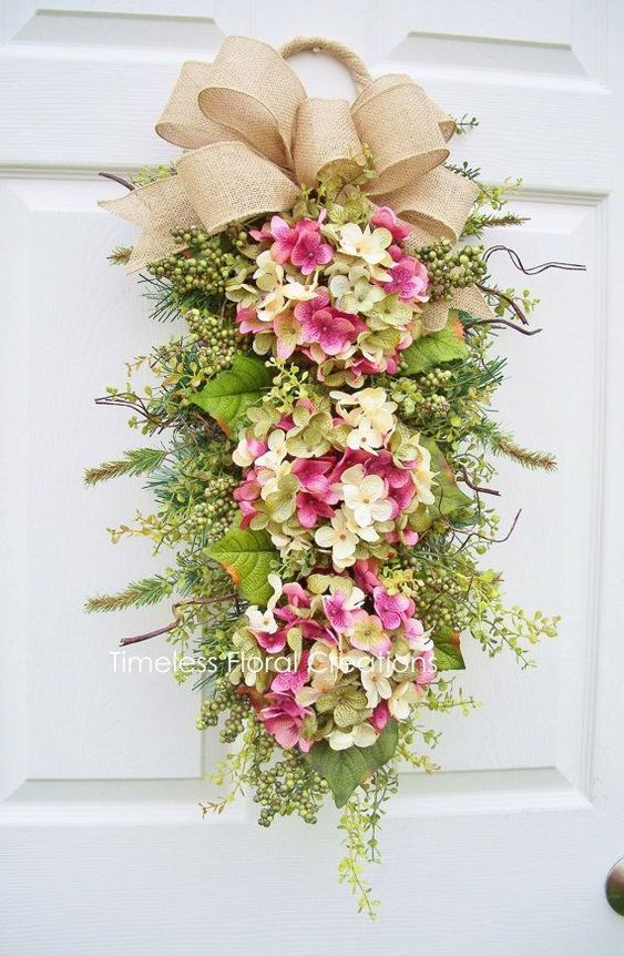 Hydrangea swag with three pink blossoms, greenery, and a burlap bow hanging on a white door.