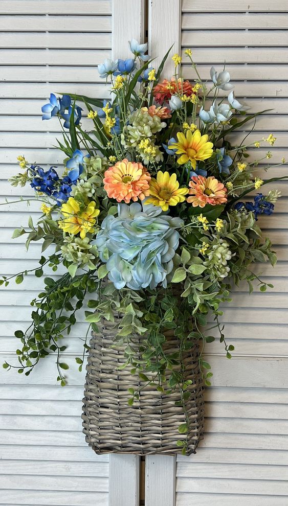 Basket of blue hydrangea, daisies and blue flowers hanging on a white louvered shutter.