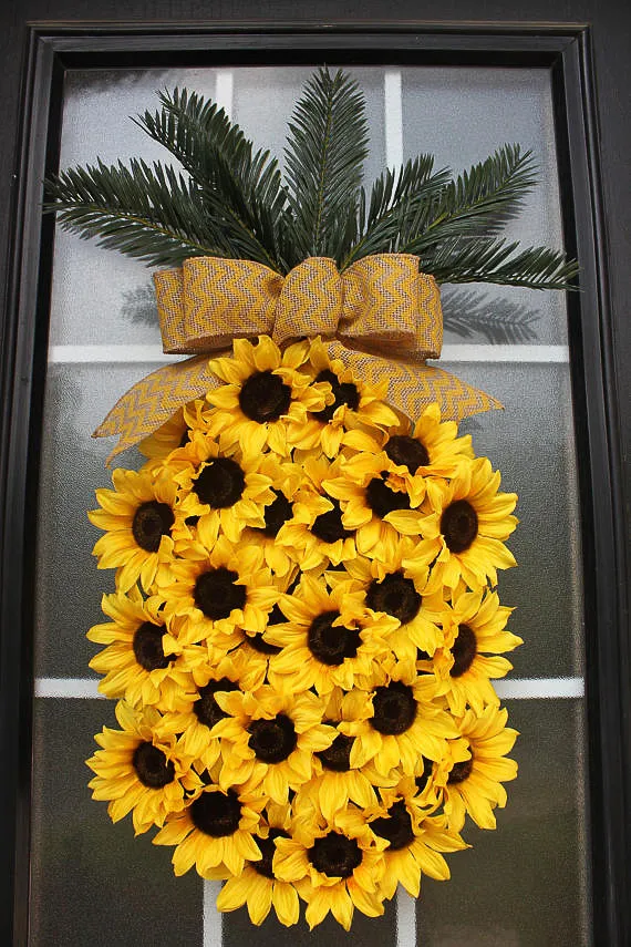 Sunflower pineapple wreath hanging on a glass door with a black frame.