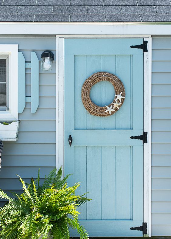 Wreath made from jute rope with three starfish attached hanging on a light blue door of a seaside cottage.