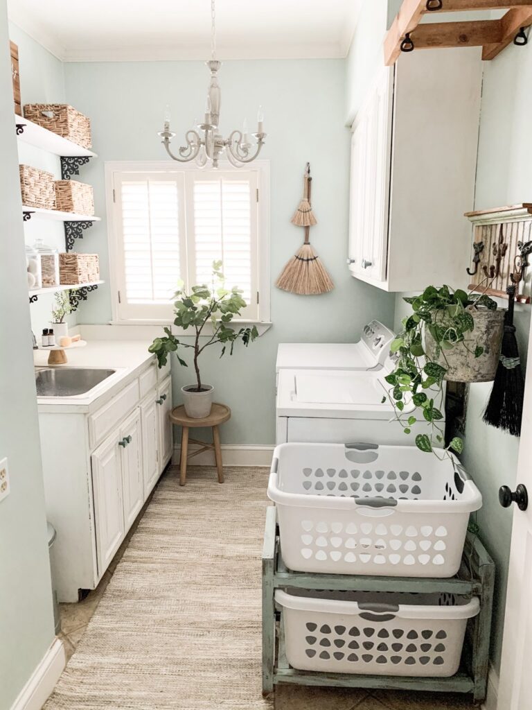 Laundry room featuring a distressed green shelving rack holding two white plastic laundry baskets stacked one over the other.