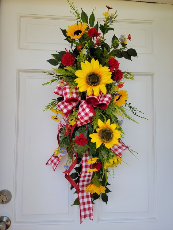 Sunflower swag with red and white checked ribbon, mini carnations, green leaves and little flowers hanging on a white door.