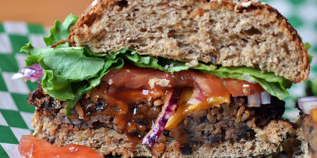 Black bean burger cut in half. Burger is on a whole grain bun with lettuce and tomato.