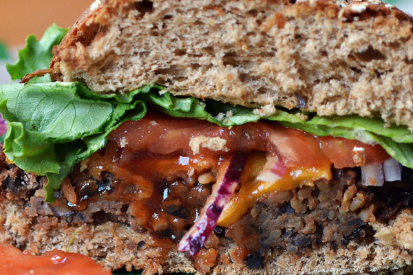 Black bean burger cut in half. Burger is on a whole grain bun with lettuce and tomato.