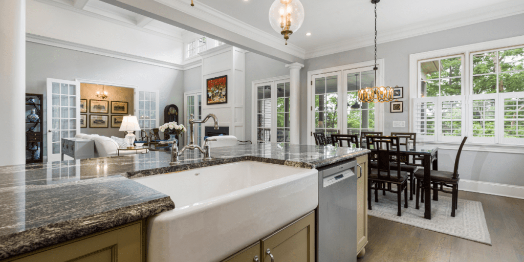 Photo of a clean kitchen with dark granite counters, white ceramic apron front sink, and coffered ceiling