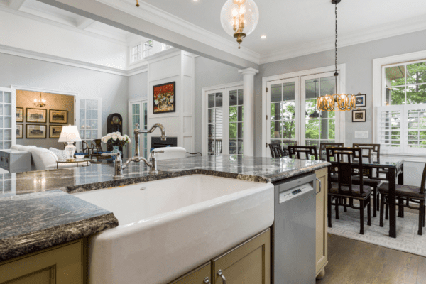 Photo of a clean kitchen with dark granite counters, white ceramic apron front sink, and coffered ceiling