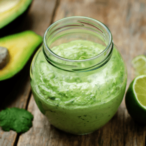 jar of cilantro lime dressing on a wood table with avocado and lime nearby