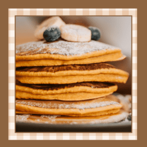 Stack of pumpkin pancakes on a plate with sliced bananas blueberries and powdered sugar on top