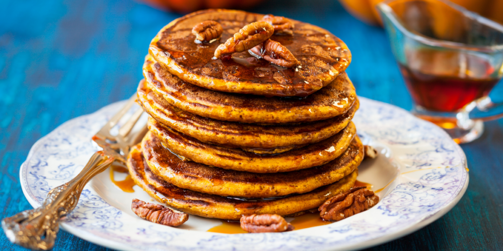 Stack of pumpkin pancakes on a plate with maple syrup and pecans.