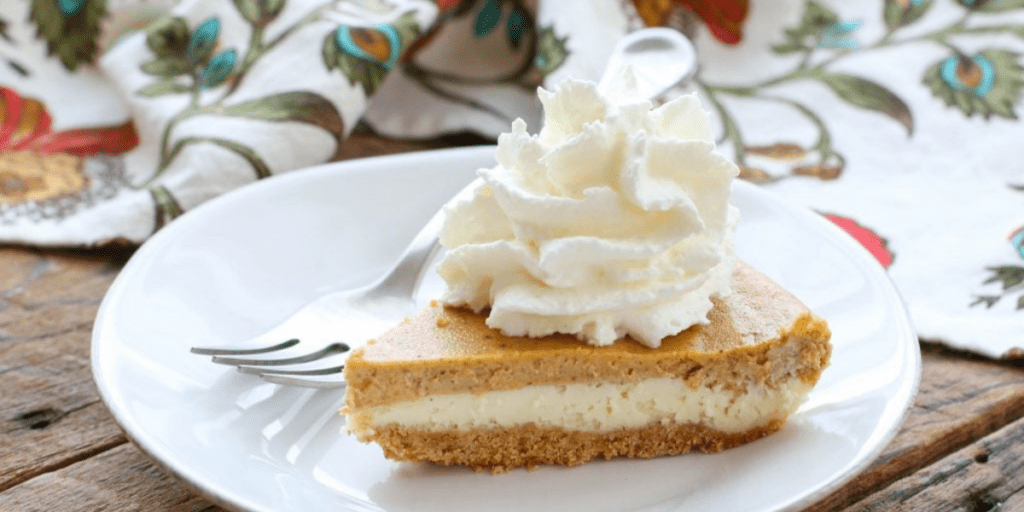 Slice of pumpkin pie cheesecake with whipped cream on a white plate.