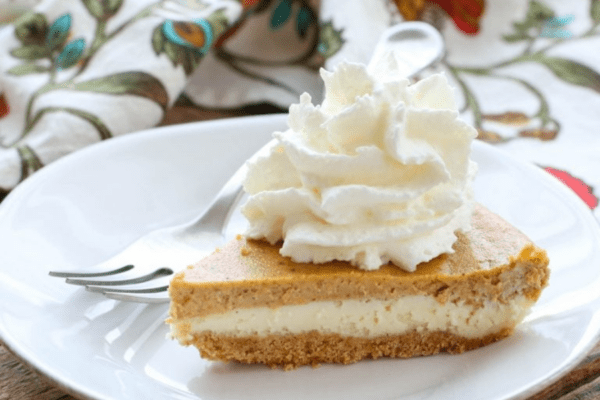 Slice of pumpkin pie cheesecake with whipped cream on a white plate.