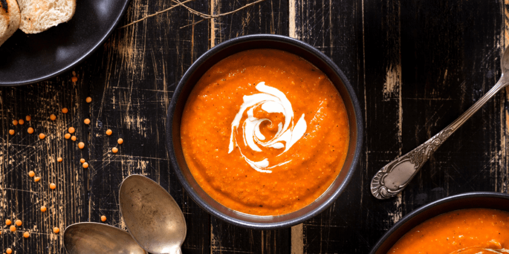 Bowl of roasted tomato soup with a splash of cream on a wood table