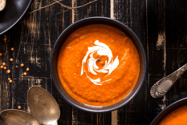 Bowl of roasted tomato soup with a splash of cream on a wood table