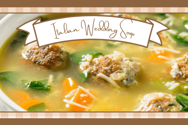 Closeup of a white bowl of wedding soup with meatballs carrots and spinach showing through the broth It sits on a blue and white striped towel with two spoons to the side