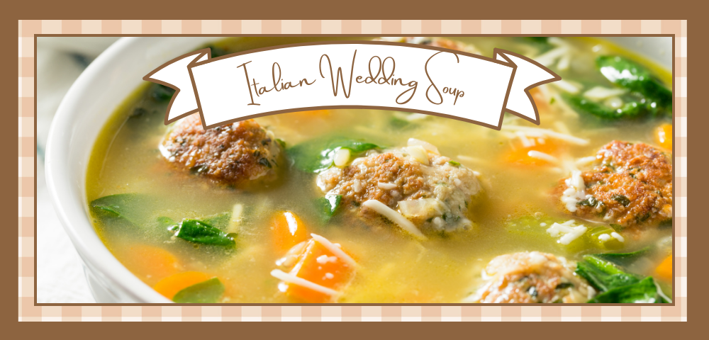 Closeup of a white bowl of wedding soup with meatballs carrots and spinach showing through the broth It sits on a blue and white striped towel with two spoons to the side