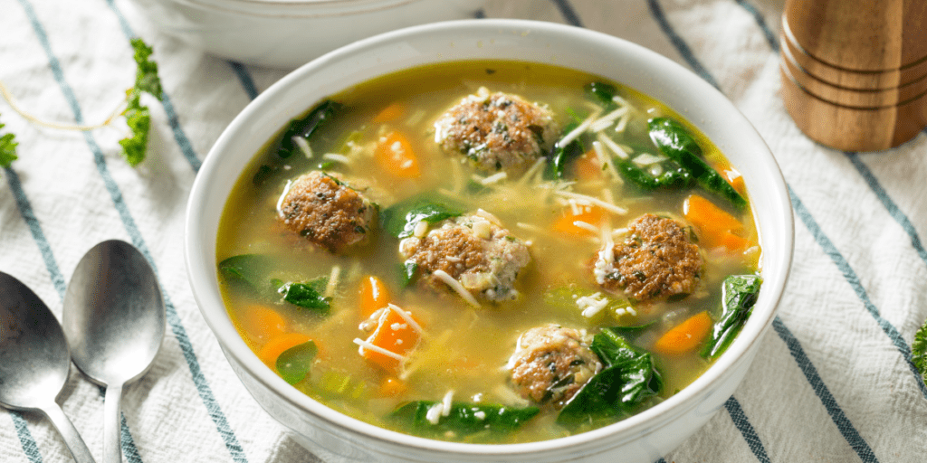 Bowl of wedding soup on a blue and white striped kitchen towel.