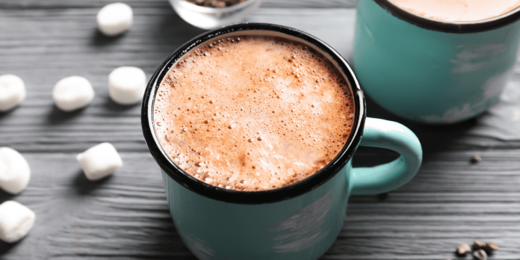 Hot cocoa in a turquoise blue mug on a gray wood table with mini marshmallows scattered around