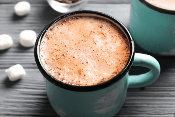 Hot cocoa in a turquoise blue mug on a gray wood table with mini marshmallows scattered around