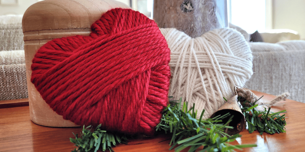 Two yarn wrapped hearts - one red and one ivory - set against two wooden candle holders.