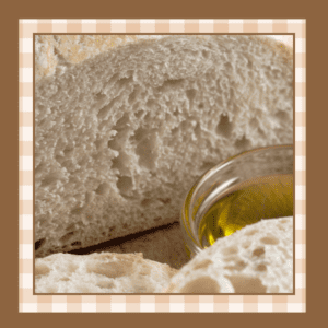 Closeup of a loaf of italian bread with some sliced off It's on a wood board with a glass dish of olive oil next to it