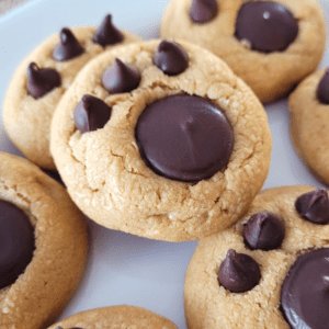 Plate of peanut butter cookies with a paw print in each one made from a chocolate disk and three chocolate chips.