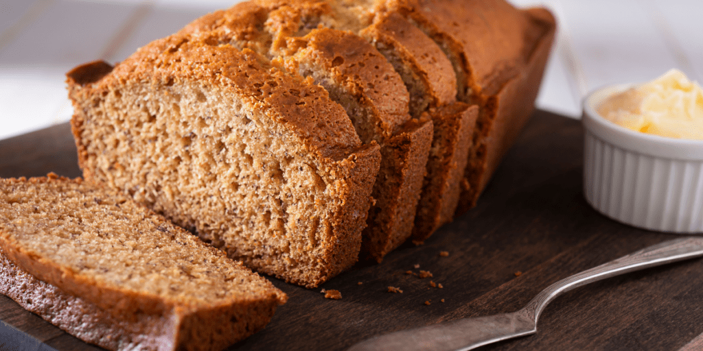 Loaf of banana bread, sliced on a cutting board with butter.