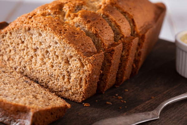 Vegan Banana Bread Banner | The Granite Acorn Loaf of banana bread sliced on a cutting board with butter