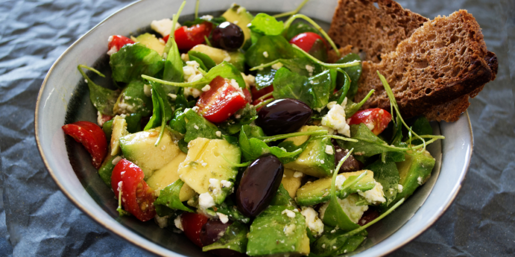 Bowl of salad with mixed greens, black olives, tomatoes, and avocado chunks.