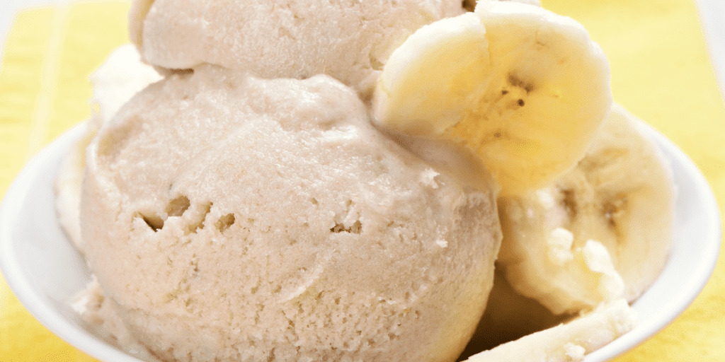 Close up of two scoops of banana ice cream in a white ceramic dish garnished with banana slices.