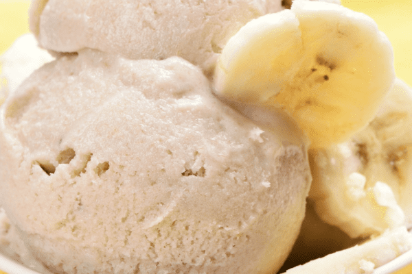 Close up of two scoops of banana ice cream in a white ceramic dish garnished with banana slices