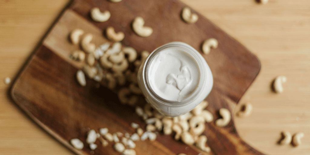 Canning jar filled with cashew cream on a wooden cutting board scattered with raw cashew nuts.